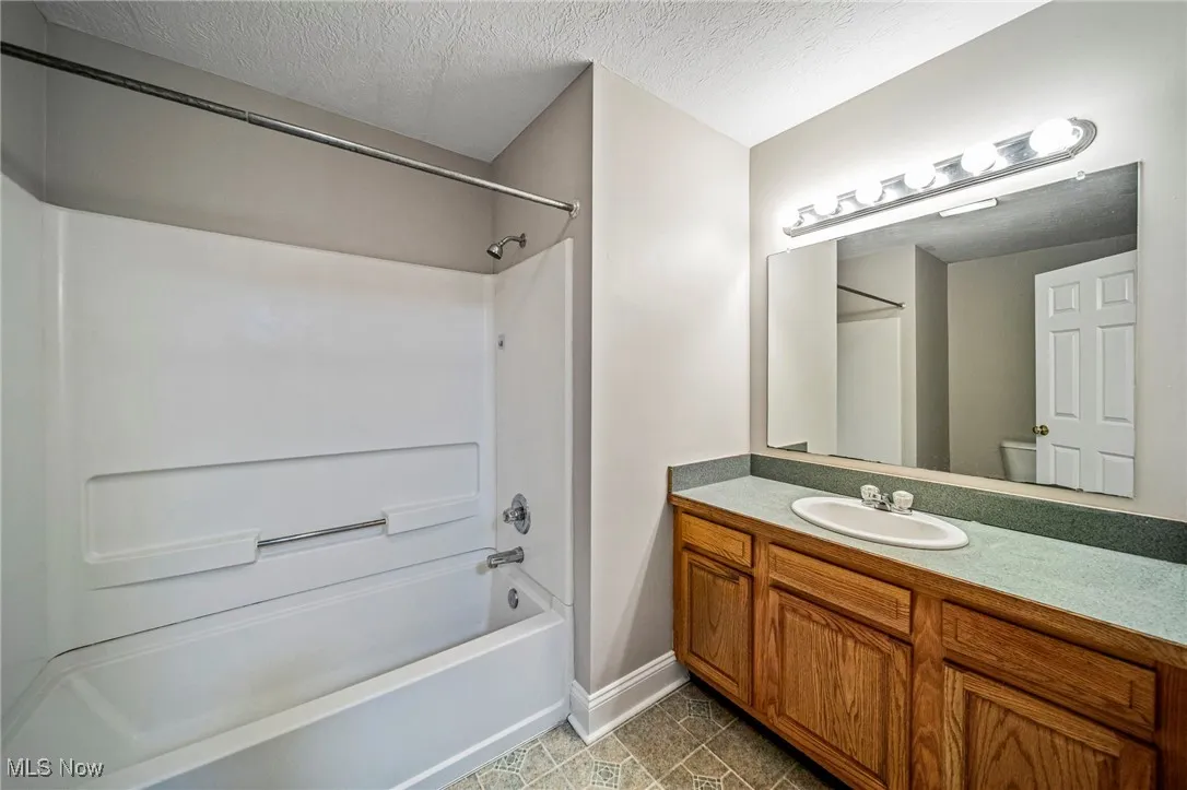 Bathroom featuring a textured ceiling, shower / tub combination, vanity, and light tile patterned floors