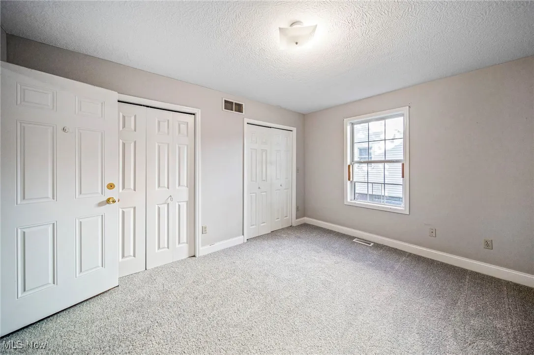 Unfurnished bedroom featuring two closets, a textured ceiling, and carpet floors
