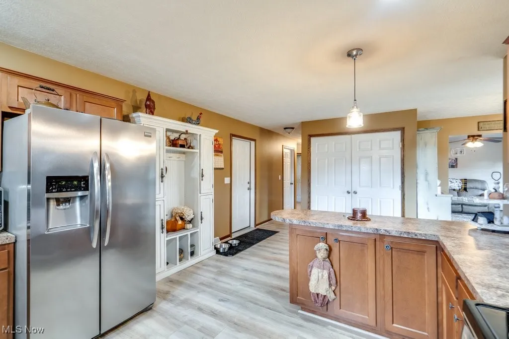 Kitchen with brown cabinets, stainless steel fridge with ice dispenser, light countertops, decorative light fixtures, and ceiling fan