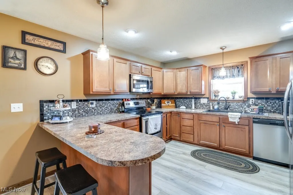 Kitchen with stainless steel appliances, a peninsula, a breakfast bar, decorative backsplash, and brown cabinets