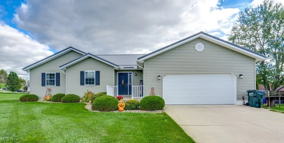 Ranch-style house with a front yard, a metal roof, a garage, and driveway