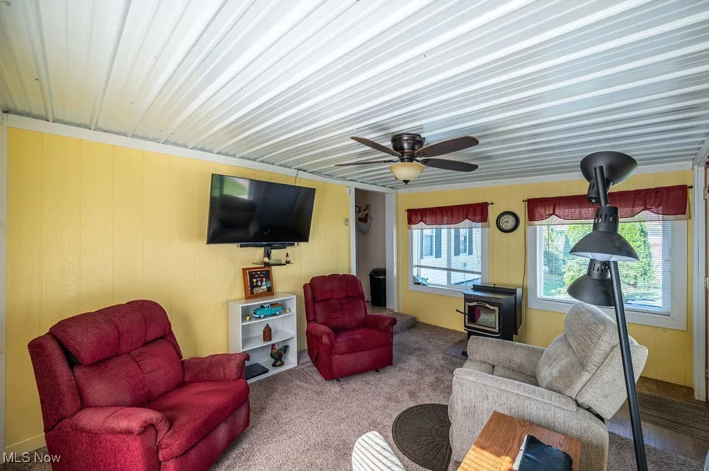 Living area with a wood stove, a ceiling fan, and carpet floors