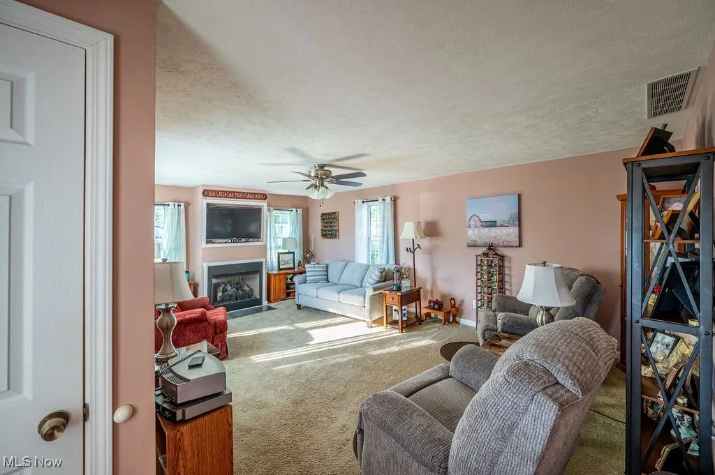 Living room featuring a textured ceiling, carpet flooring, a fireplace with flush hearth, and ceiling fan