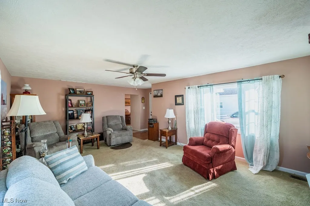 Carpeted living room featuring ceiling fan and a textured ceiling