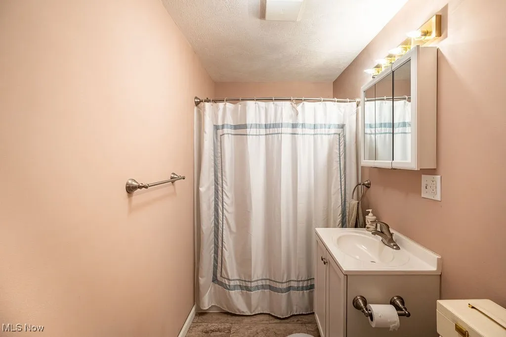 Bathroom featuring a textured ceiling, vanity, and curtained shower