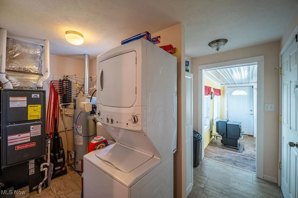 Laundry room featuring a textured ceiling, heating unit, stacked washer and clothes dryer, and water heater