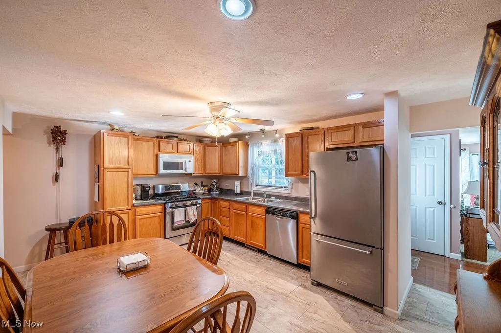 Kitchen with stainless steel appliances, a textured ceiling, recessed lighting, ceiling fan, and brown cabinets