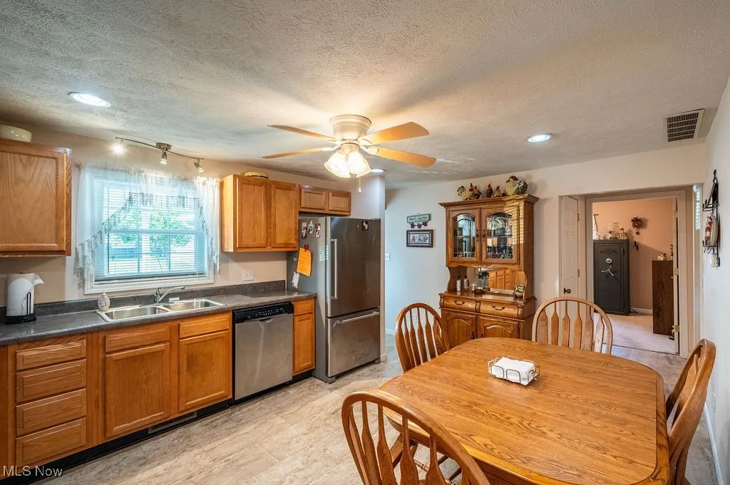Kitchen featuring dark countertops, brown cabinetry, appliances with stainless steel finishes, a ceiling fan, and a textured ceiling