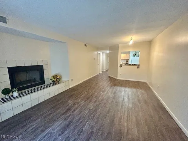 Unfurnished living room with a tiled fireplace, dark wood-type flooring, and a textured ceiling