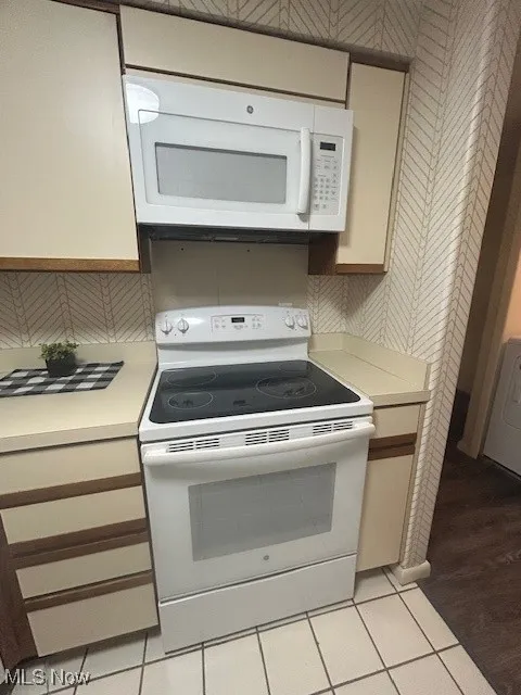 Kitchen with electric stove, light countertops, stainless steel microwave, light tile patterned floors, and washer / dryer