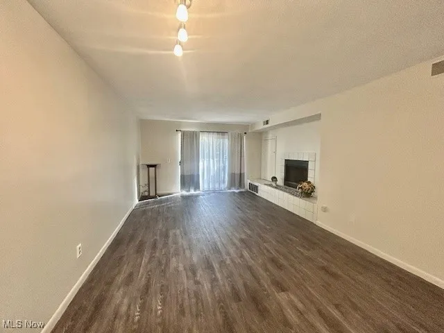 Unfurnished living room featuring a tile fireplace, dark wood-style flooring, and a textured ceiling
