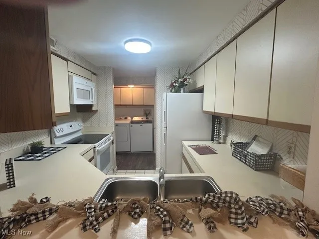 Kitchen with white appliances, light countertops, washer and clothes dryer, and wood finished floors