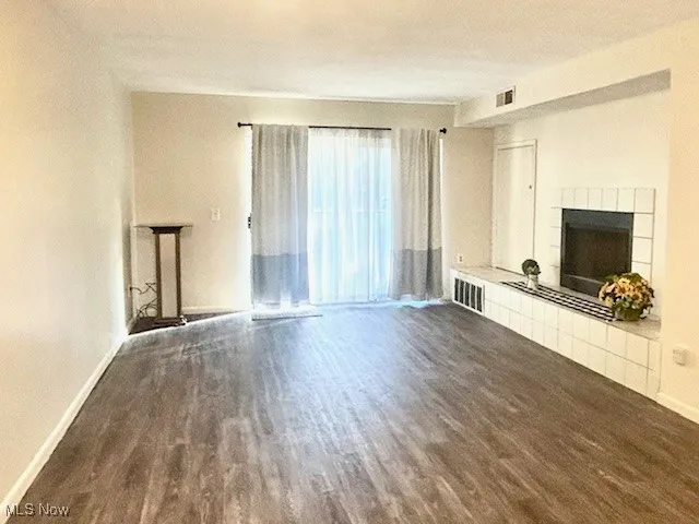 Unfurnished living room featuring a tiled fireplace and dark wood-style floors
