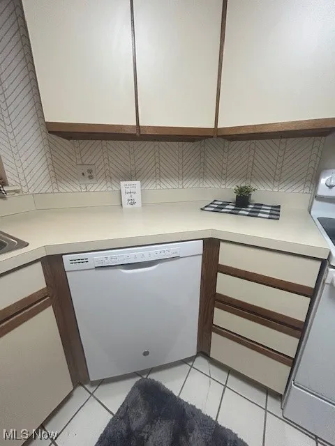 Kitchen featuring light countertops, dishwasher, light tile patterned flooring, stove, and white cabinetry