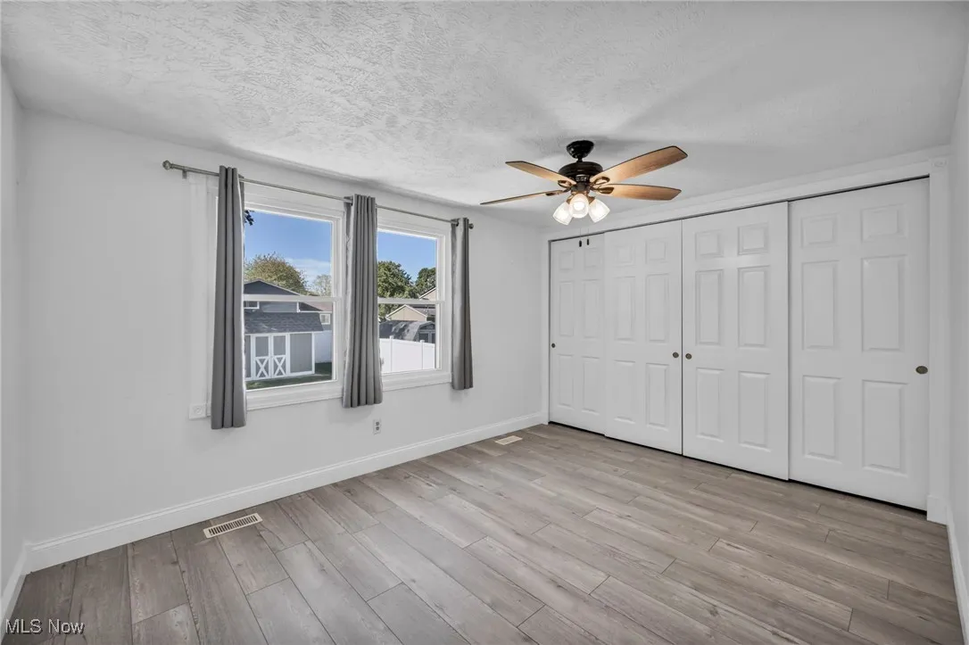 Unfurnished bedroom with a textured ceiling, a ceiling fan, a closet, and light wood-style floors