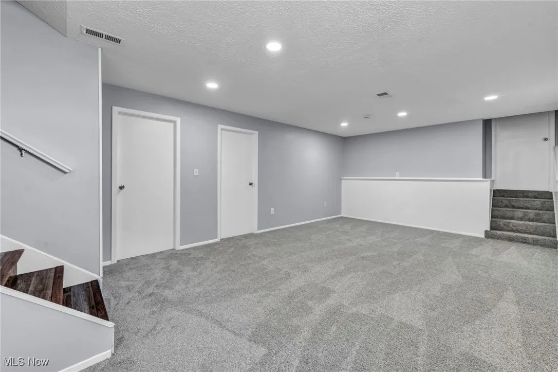 Finished basement featuring stairs, a textured ceiling, light carpet, and recessed lighting