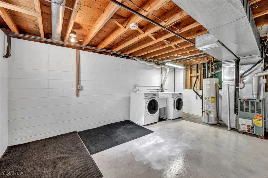 Unfinished below grade area featuring heating unit, water heater, and washing machine and clothes dryer