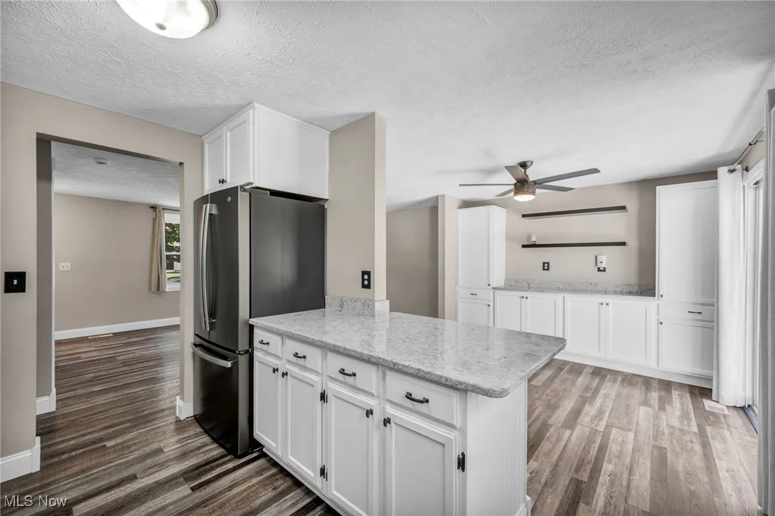 Kitchen with white cabinetry, a textured ceiling, freestanding refrigerator, light stone countertops, and dark wood-type flooring