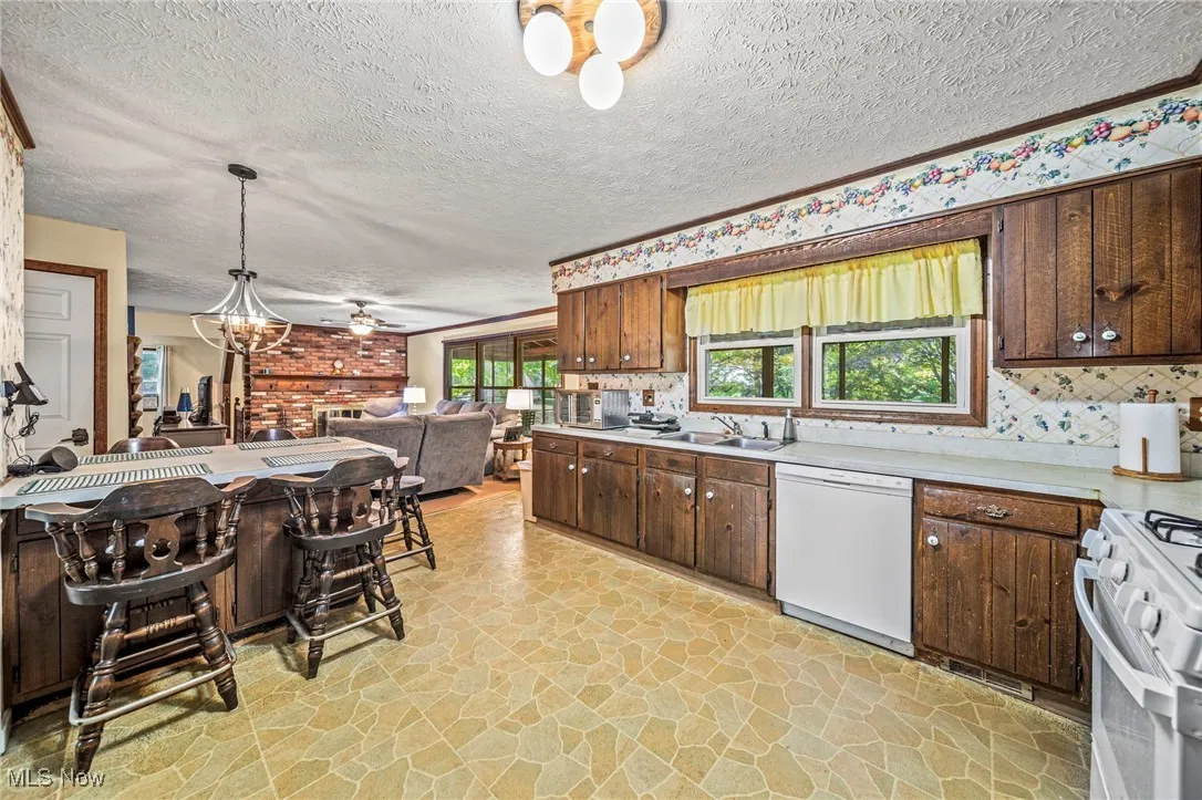 Kitchen with light stone finish floors, white appliances, light countertops, dark brown cabinets, and decorative light fixtures