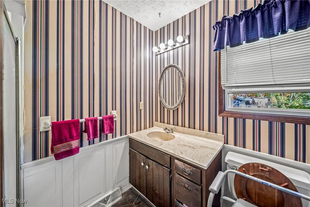 Bathroom with wallpapered walls, vanity, and a textured ceiling