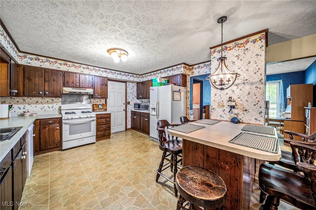 Kitchen featuring dark brown cabinets, white appliances, light countertops, hanging light fixtures, and a textured ceiling