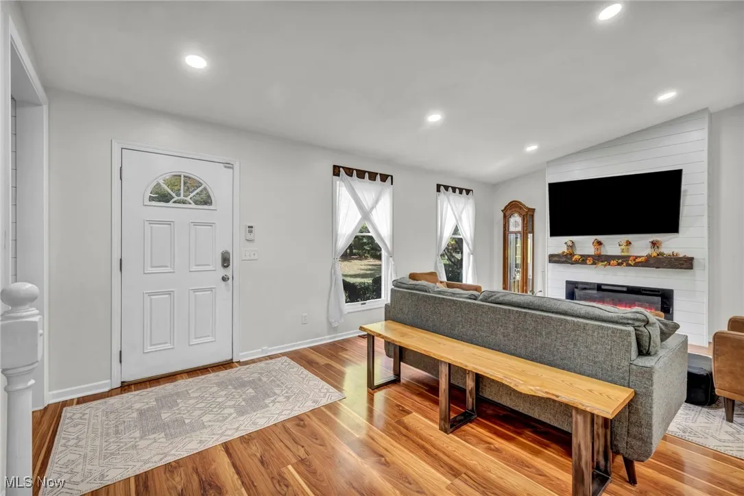 Living area with vaulted ceiling, light wood finished floors, recessed lighting, and a glass covered fireplace
