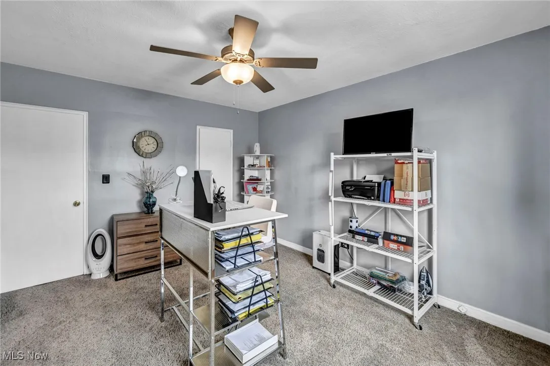 Carpeted office space with ceiling fan and baseboards
