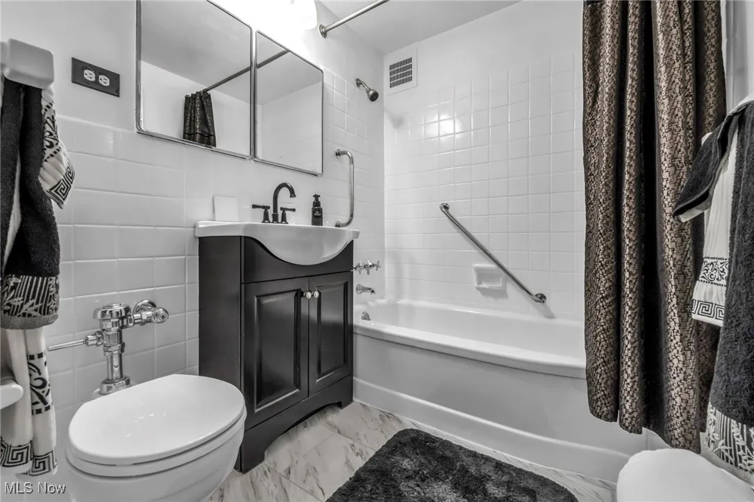 Bathroom with shower / bath combo with shower curtain, vanity, and marble look tile flooring