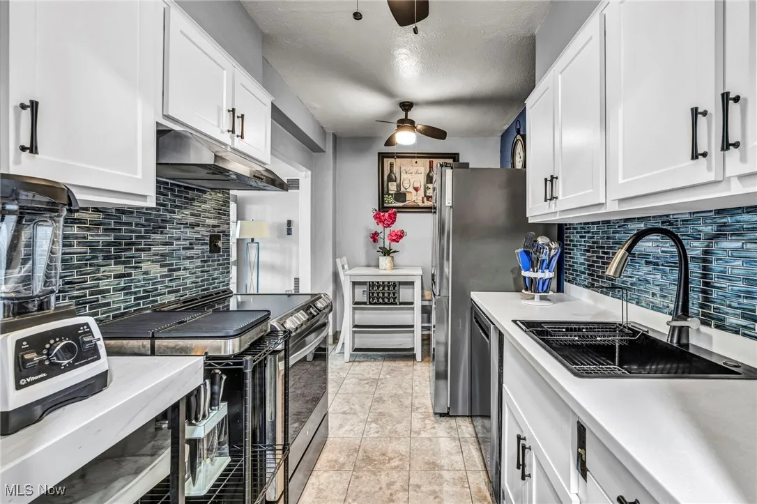 Kitchen featuring stainless steel appliances, under cabinet range hood, a ceiling fan, light countertops, and white cabinetry