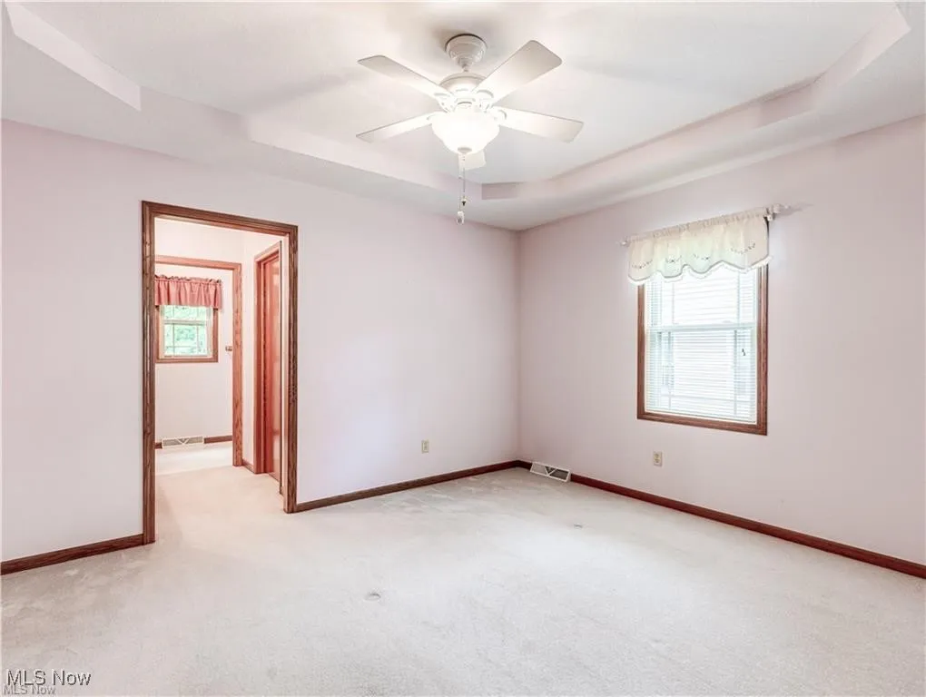 Primary bedroom with carpet, ceiling fan / light, Tray ceiling and showing the door to primary bath