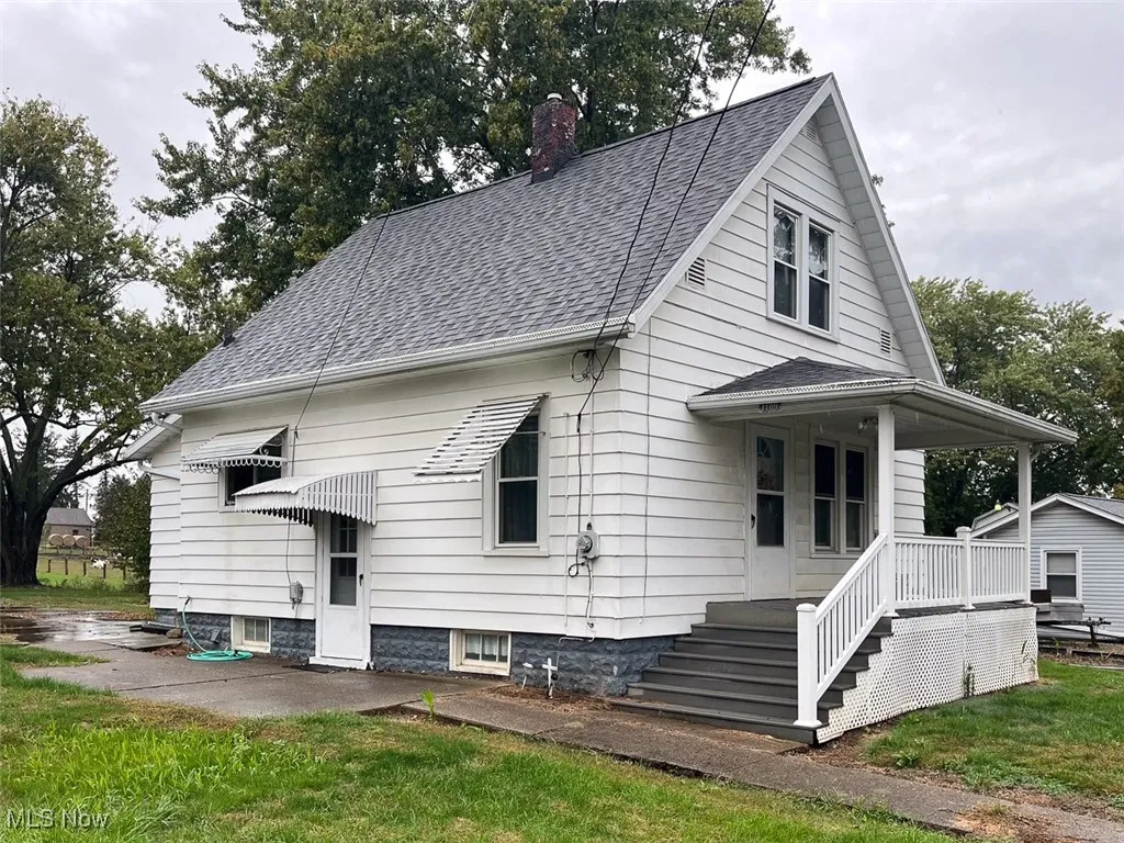 Side view of property featuring a chimney, roof with shingles, a porch, and a lawn