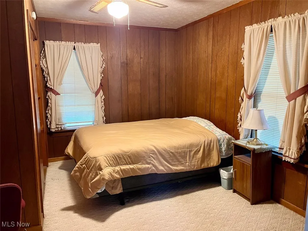 Bedroom with wood walls, carpet, a textured ceiling, and a ceiling fan