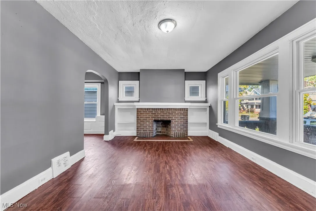 Unfurnished living room featuring dark wood-type flooring, a textured ceiling, arched walkways, and a brick fireplace