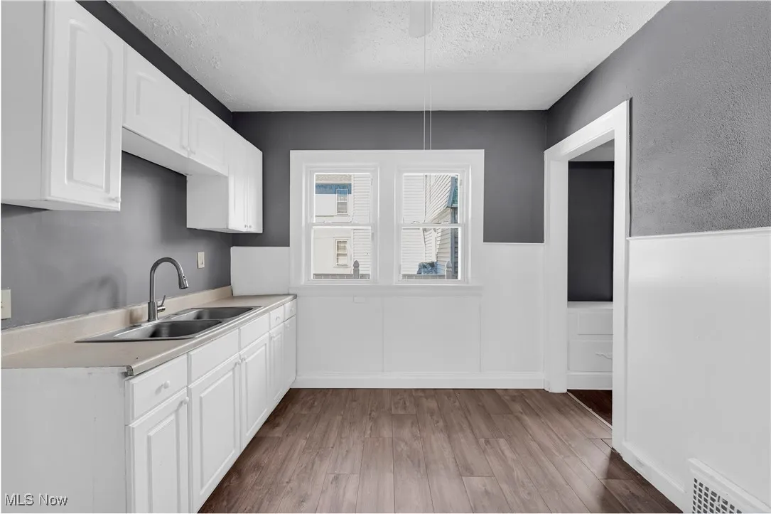 Kitchen with white cabinetry, light wood-type flooring, light countertops, a textured ceiling, and a wainscoted wall