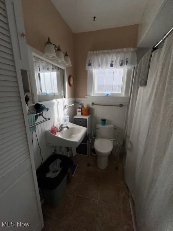 Bathroom featuring a wainscoted wall, dark tile patterned flooring, and a shower with curtain