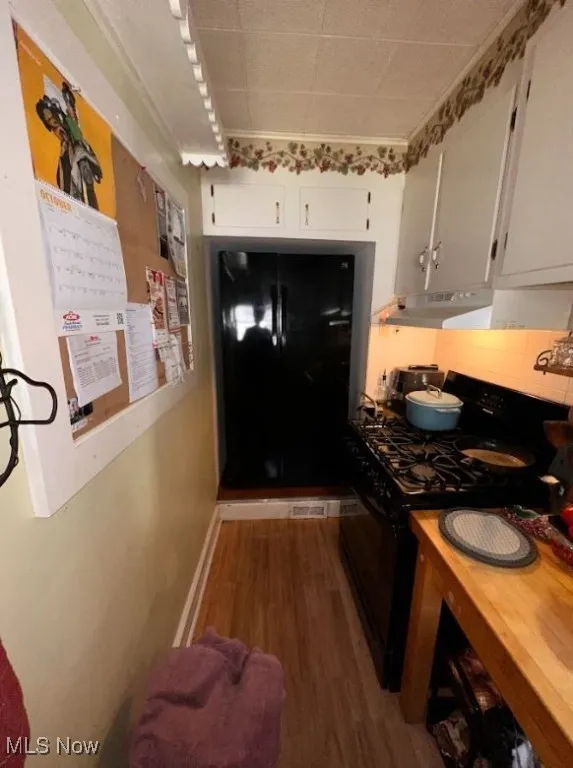 Kitchen with black range with gas stovetop, dark wood-style floors, backsplash, white cabinets, and butcher block counters