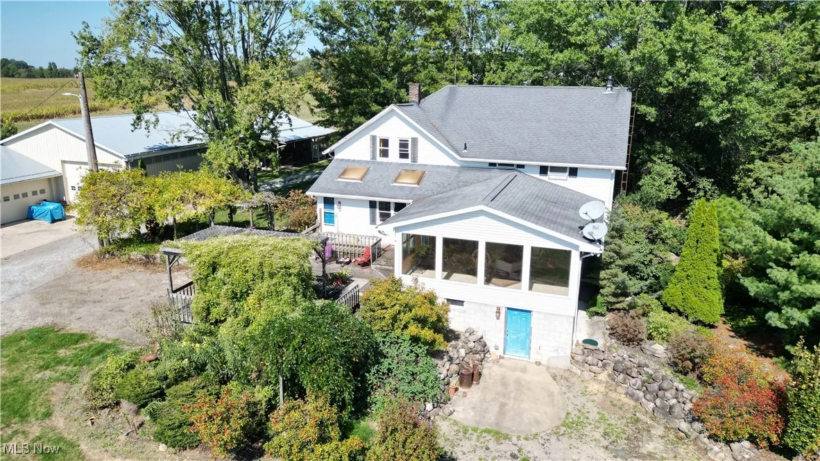 Back of house featuring a sunroom, a shingled roof, a chimney, and view of scattered trees
