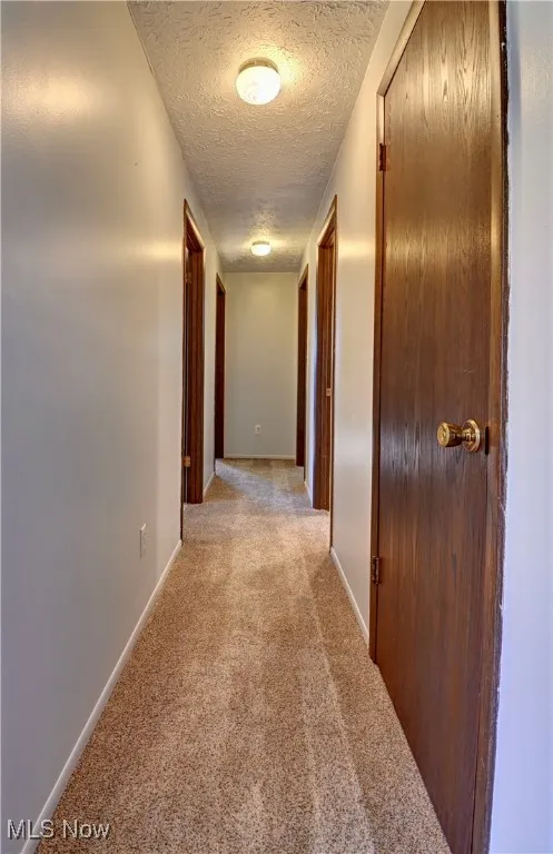 Hallway featuring a textured ceiling and light colored carpet