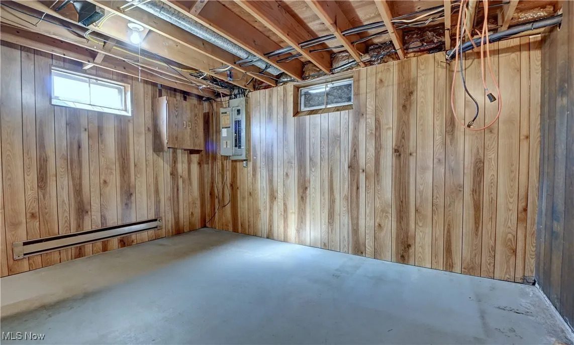 Below grade area featuring a baseboard radiator, wood walls, and electric panel