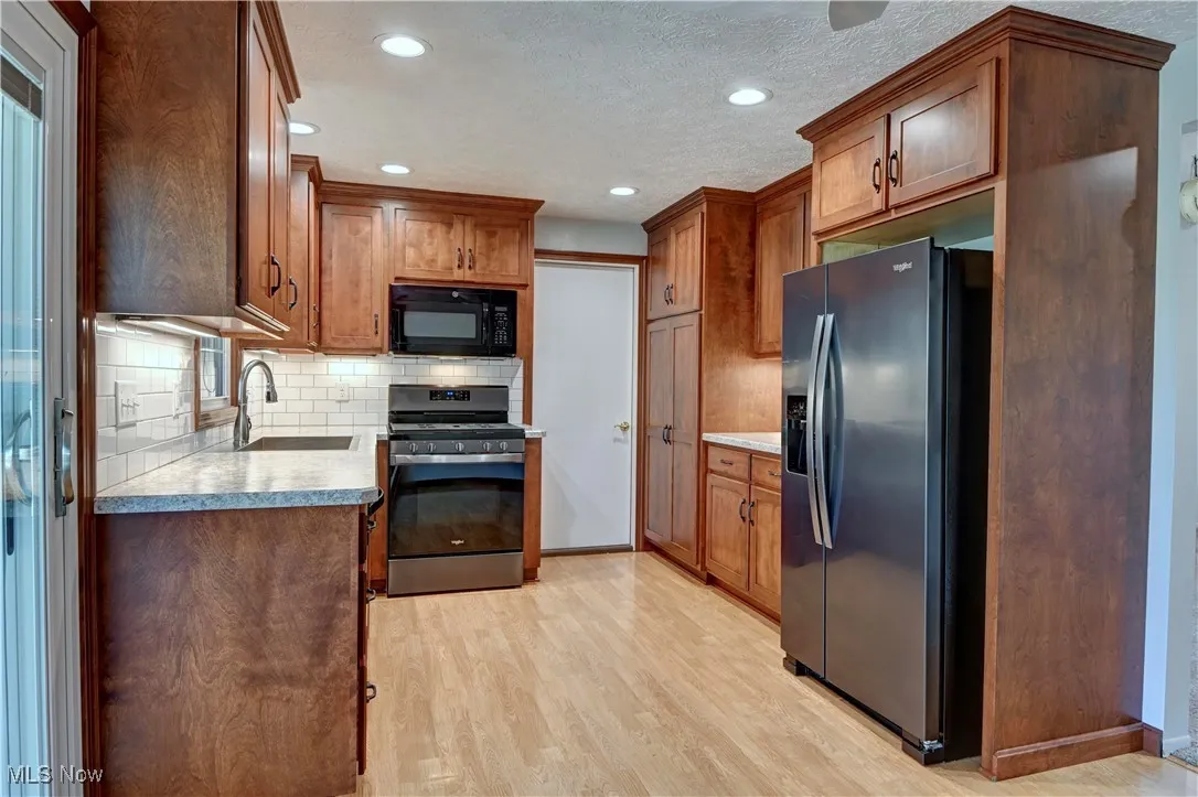 Kitchen featuring stainless steel appliances, decorative backsplash, brown cabinetry, light wood-type flooring, and a textured ceiling