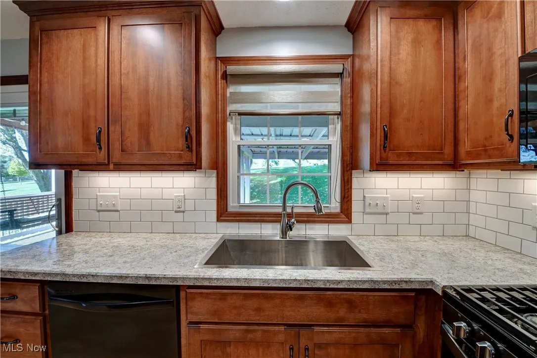 Kitchen featuring black appliances, brown cabinets, light stone countertops, and decorative backsplash