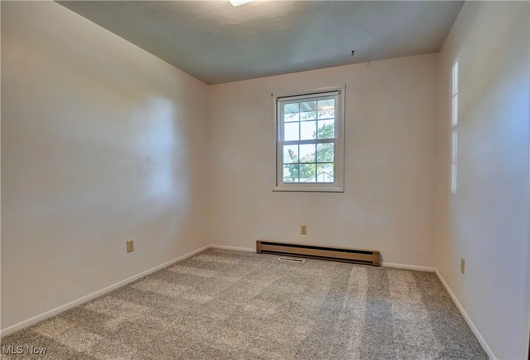 Carpeted empty room with a baseboard radiator and baseboards