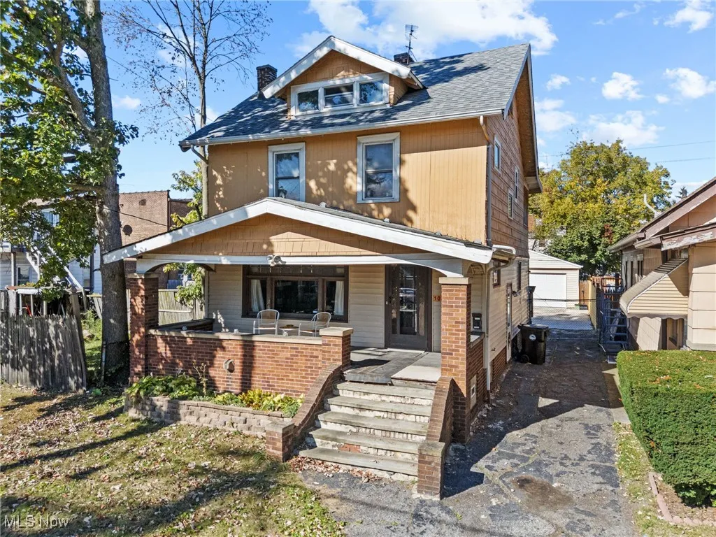 American foursquare style home with covered porch, roof with shingles, an outbuilding, and a garage