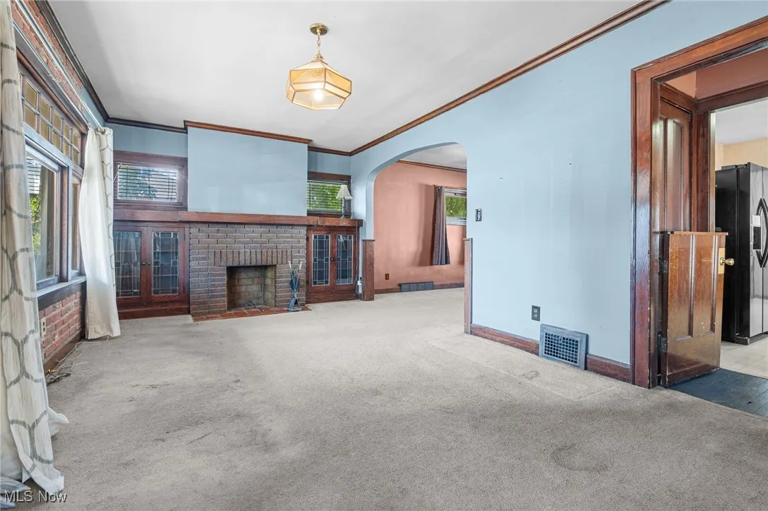Unfurnished living room with ornamental molding, carpet floors, a fireplace, and arched walkways