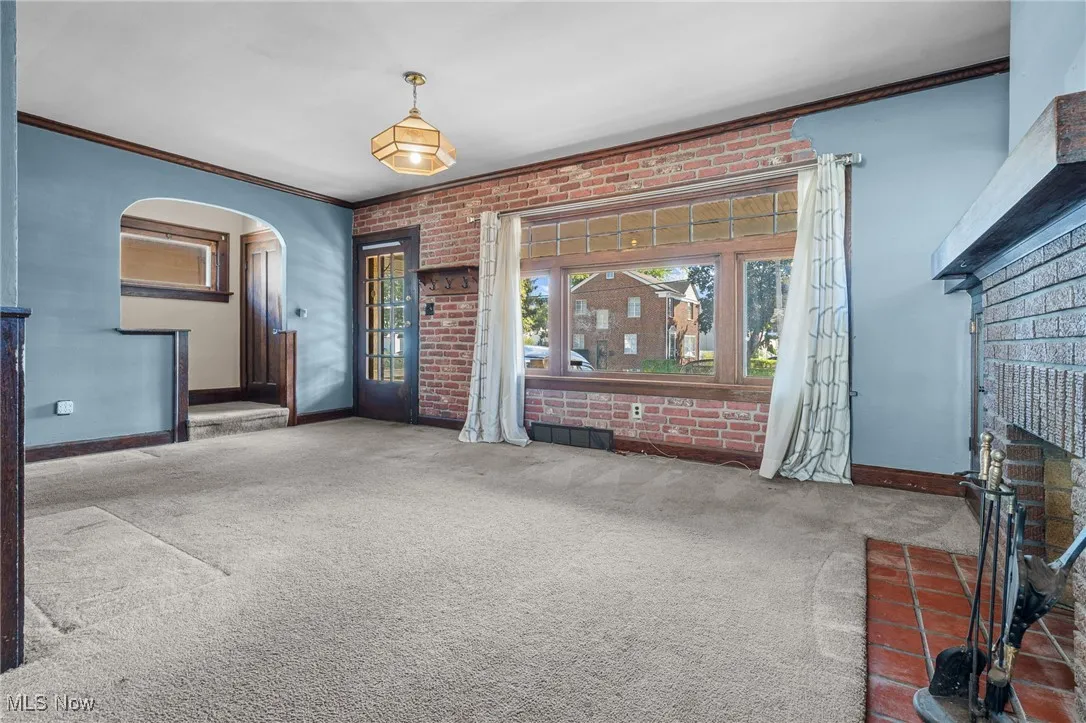 Unfurnished living room with brick wall, crown molding, arched walkways, carpet flooring, and a brick fireplace