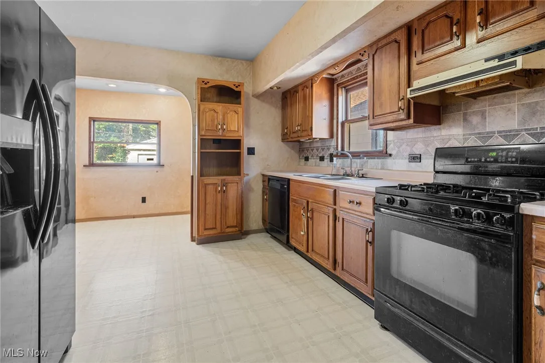 Kitchen with black appliances, light flooring, brown cabinets, and light countertops