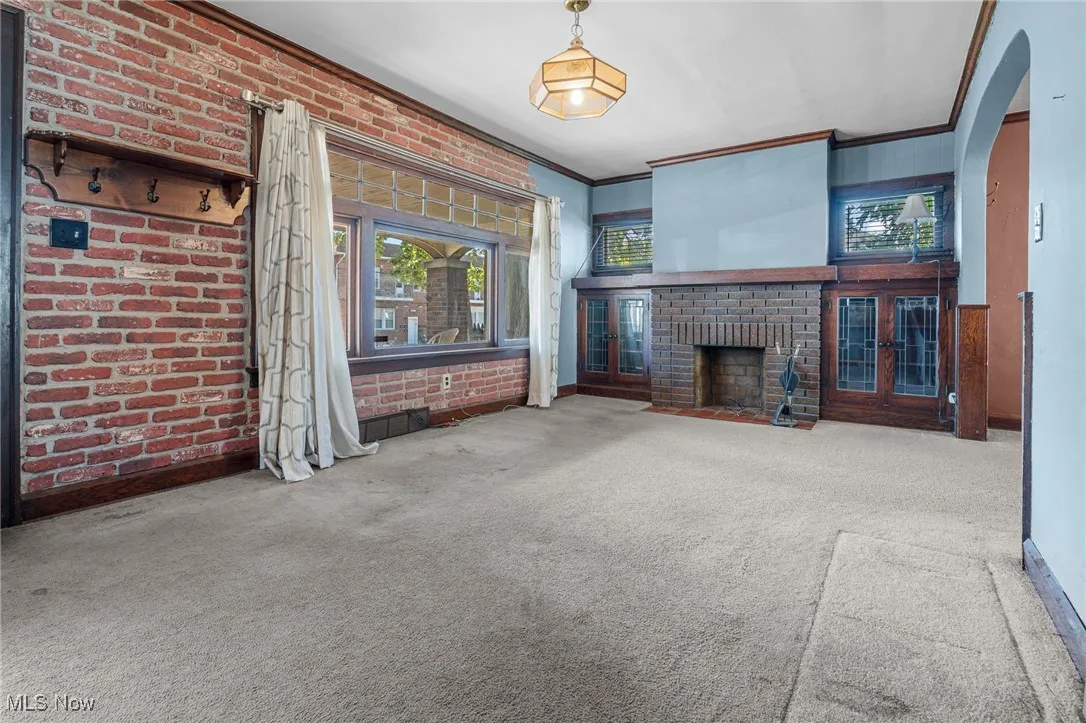 Unfurnished living room featuring brick wall, arched walkways, ornamental molding, carpet, and a brick fireplace