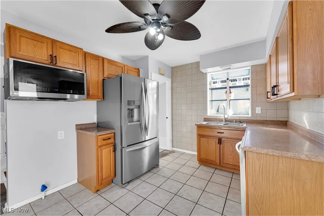 Kitchen featuring appliances with stainless steel finishes, tile walls, light tile patterned floors, light countertops, and ceiling fan