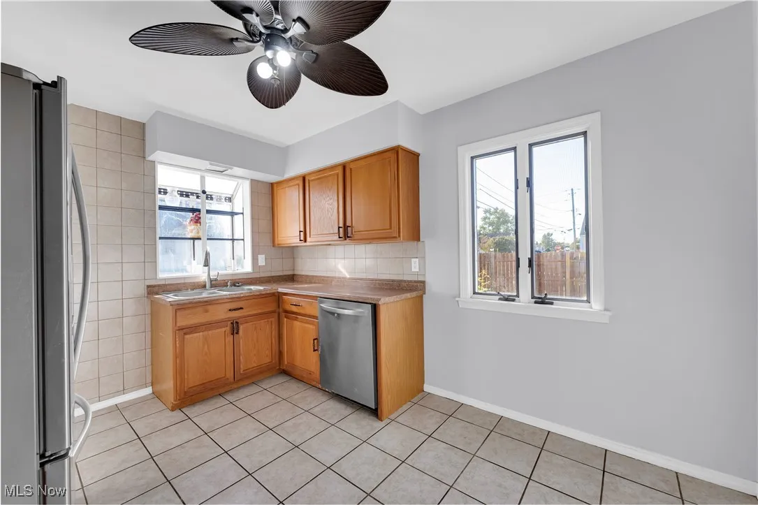 Kitchen featuring stainless steel appliances, light tile patterned flooring, light countertops, brown cabinets, and a ceiling fan