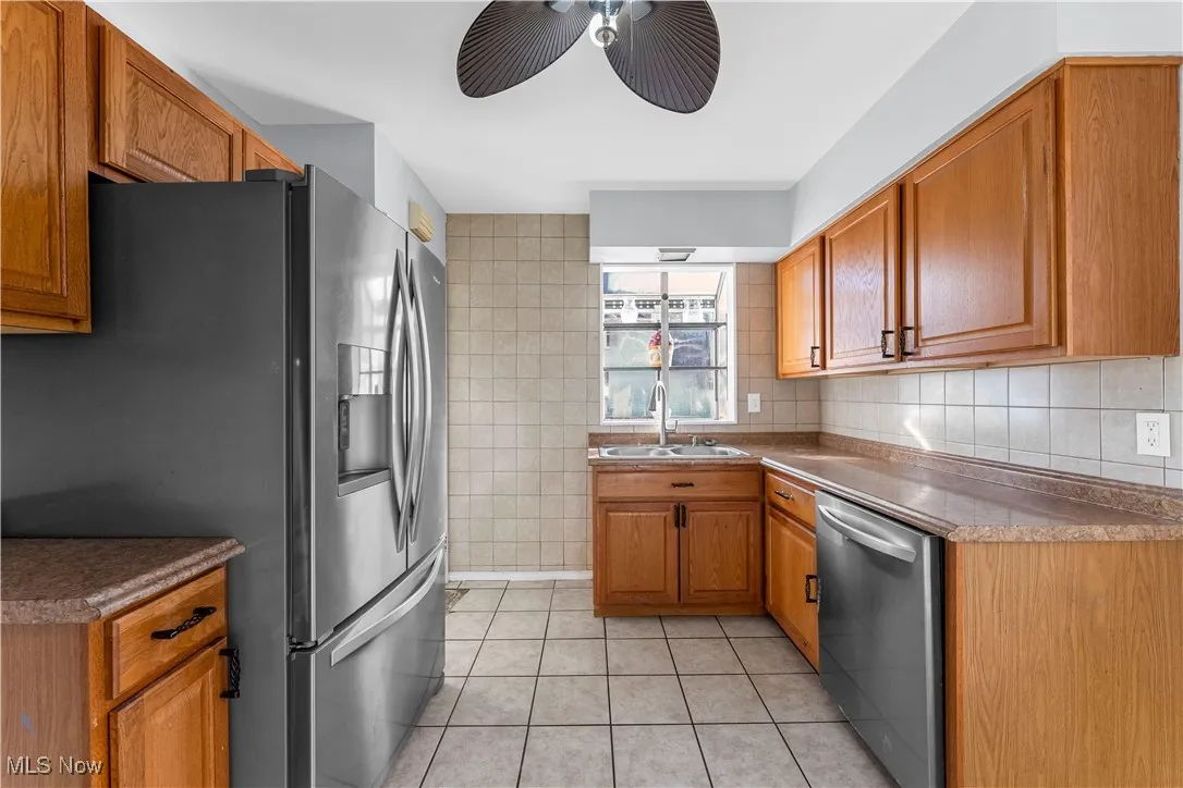 Kitchen featuring tile walls, light tile patterned floors, brown cabinets, stainless steel appliances, and dark countertops